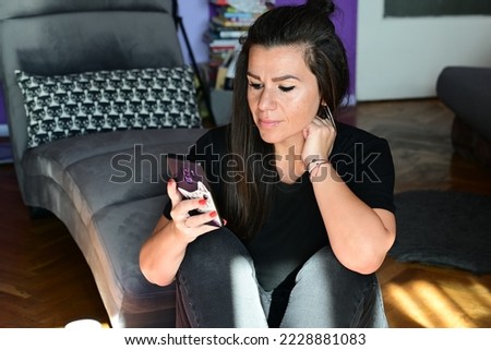Beautiful smiling woman sitting on the carpet at home    looking at the phone  reading a Message ,checking social media  using mobile phone app playing game, shopping online, ordering delivery 