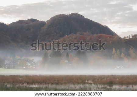 Stunning Autumn landscape sunrise image looking towards Borrowdale Valley from Derwentwater in Lake District with fog rolling across the landscape