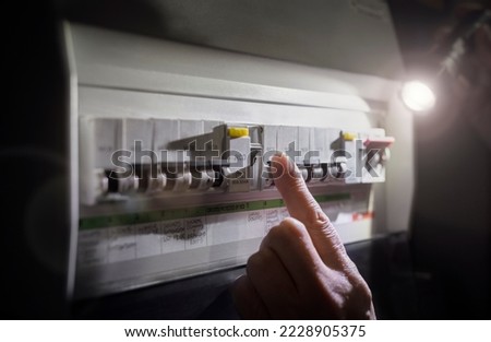 Electricity power outage emergency turning on or off circuit breaker on electrical fuse board with flashlight Royalty-Free Stock Photo #2228905375