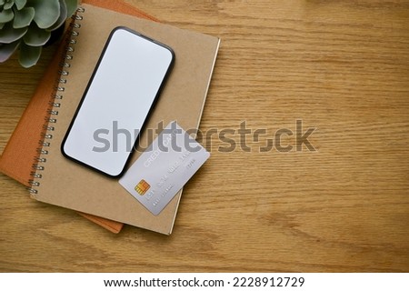 Workspace tabletop with smartphone white screen mockup, credit card, books, and copy space on rustic wood background. top view