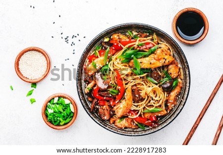 Stir fry egg noodles with chicken, sweet paprika, mushrooms, chives and sesame seeds in bowl. Asian cuisine dish. White table background, top view Royalty-Free Stock Photo #2228917283