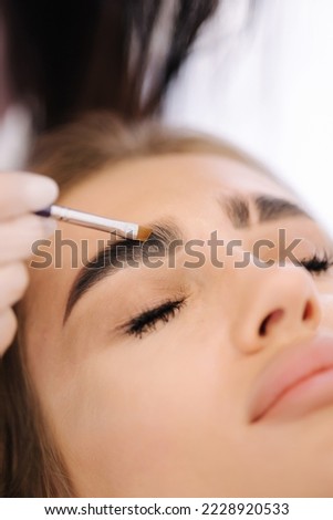 Brow master applies henna on eyebrows for beautiful blond hair woman. Fashion slyle Royalty-Free Stock Photo #2228920533