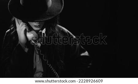 Dark noir portrait of a female detective holding a retro telephone receiver. Private detective, spy, investigation concept. black and white snapshot