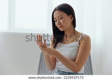 Broken hand Cramp. Upset suffering tanned beautiful young Asian woman touching massaging painful hand wrist at home interior living room. Injuries Poor health Illness concept. Cool offer Banner Royalty-Free Stock Photo #2228929173