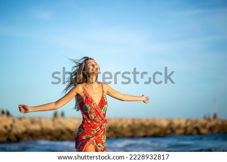 Portrait carefree young woman standing with arms raised by beach