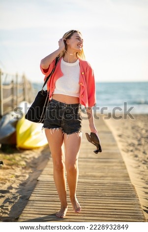 Full body portrait young woman walking barefoot by beach