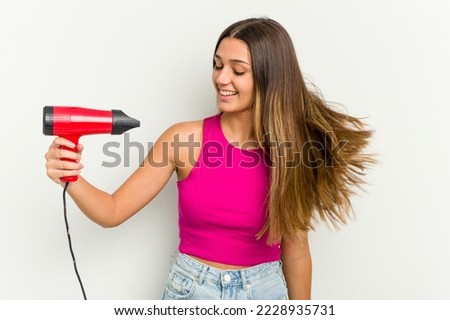 Young Indian woman holding a hairdryer isolated on white background Royalty-Free Stock Photo #2228935731