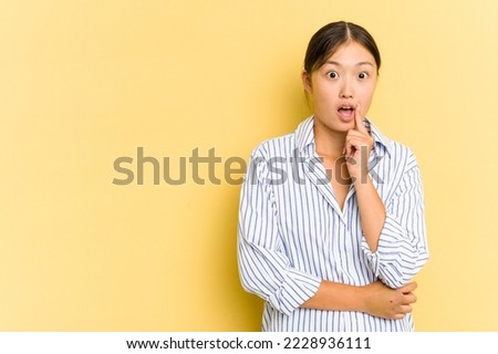 Young Asian woman isolated on yellow background looking sideways with doubtful and skeptical expression.