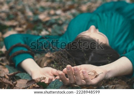 Close up lady lying on ground concept photo. Autumn forest. Palms up. Side view photography with green dress on background. High quality picture for wallpaper, travel blog, magazine, article