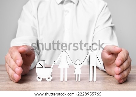 Man protecting figures of family at wooden table. closeup. Insurance concept