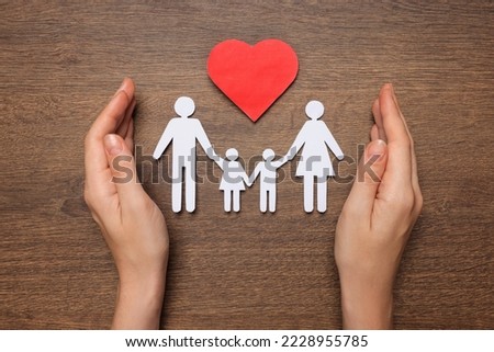 Woman protecting paper family cutout at wooden table, top view. Insurance concept Royalty-Free Stock Photo #2228955785