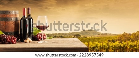 Red wine bottles, wine glass, barrel, grapes and vineyard in the background: wine making and wine tasting experience, banner with copy space