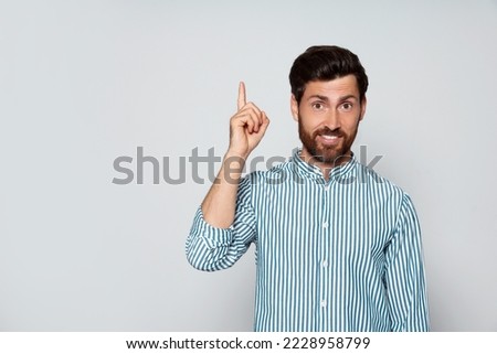Bearded man pointing index finger up on grey background. Space for text