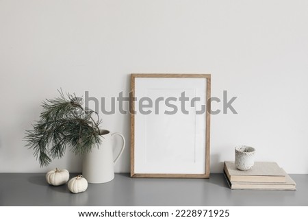 Christmas interior decor, still life. Blank wooden picture frame mockup. Vase with pine tree branches, cup of coffee and old books on grey desk. Winter home office. White little pumkins on table.