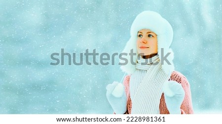 Portrait of young woman wearing hat, sweater and scarf on snowy forest background with snowflakes, blank copy space for advertising text