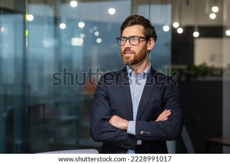 Portrait of successful mature investor, senior businessman inside office looking towards window smiling with crossed arms, man in glasses and business suit. Royalty-Free Stock Photo #2228991017