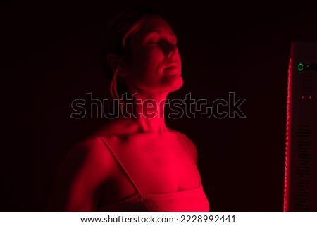 Woman getting red light therapy in a beauty salon. Mature woman getting anti-aging treatment from a red light device. Skin care and rejuvenation procedure. Royalty-Free Stock Photo #2228992441
