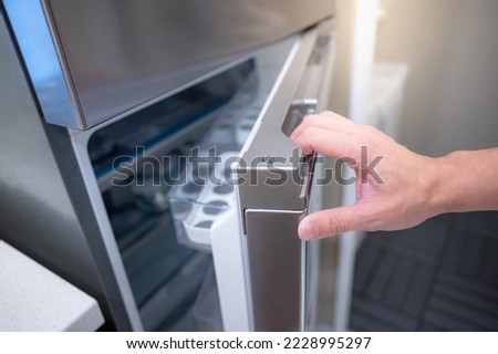 Male hand opening fridge or refrigerator door in kitchen showroom. Buying appliance for home interior design. Royalty-Free Stock Photo #2228995297
