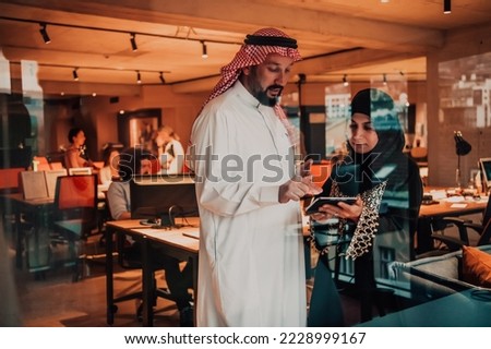Portrait photo of Arab leader businessman with muslim hijab woman discussing business projects while using tablets and smartphone in modern glass office 