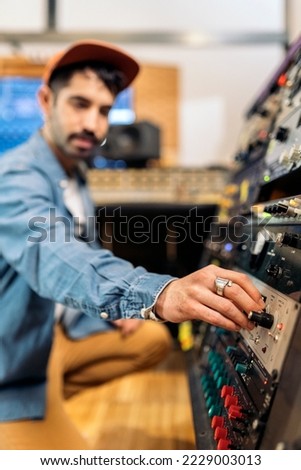 Stock photo of hipster man using panel control in professional music studio.