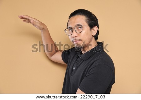 Asian male in black shirt pointing at a direction over isolated studio background.