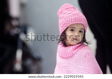 2 years old Indian baby dressed in pink winter cap and poncho looking at the camera innocently.