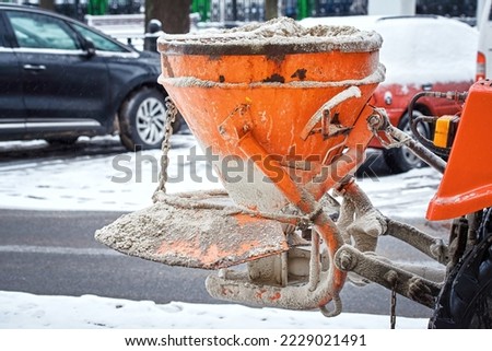 Salt spreader, tactor spreading rock salt on sand on sidewalk, winter road maintenance, prevent slipping.Tractor de-icing street, spread salt reagent. Municipal service melt ice. Bucket with salt