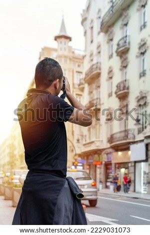 Man from the back holding a photo camera taking a photo of a city street in sunset light