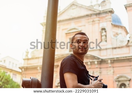Latin man traveler holding a photo camera with an old church out of focus in the background