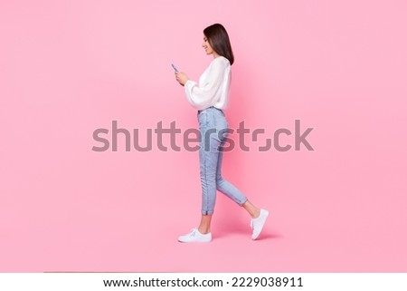 Full size photo of stunning young woman walking hold gadget reading news repost wear trendy white garment isolated on pink color background
