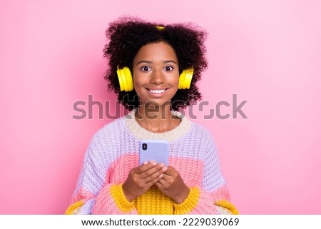 Photo of positive cheerful optimistic girl perming coiffure wear knit sweater headphones hold smartphone isolated on pink color background