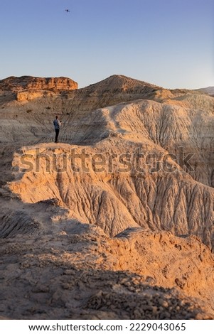 Young adult man flying drone in semi-desert area with erosional figures and cliffs. Vertical photography