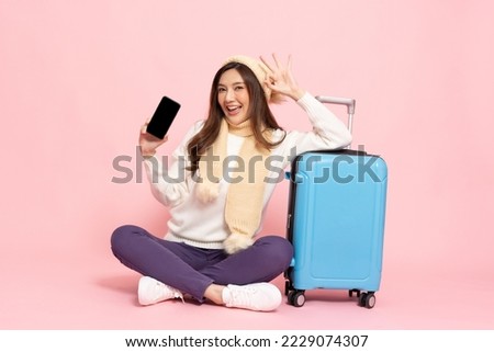 Happy Asian woman traveler sitting on floor with luggage and holding mobile phone isolated on pink background, Tourist girl having cheerful holiday trip concept, Full body composition Royalty-Free Stock Photo #2229074307