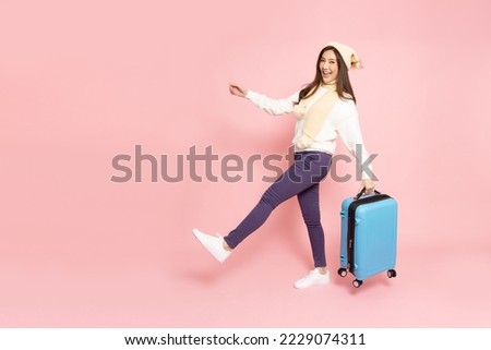 Happy Asian woman traveler walking and holding luggage isolated on pink background, Tourist girl having cheerful holiday trip concept, Full body composition