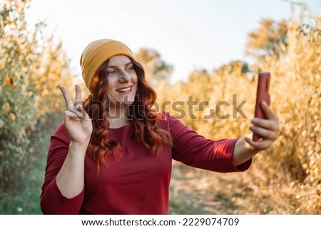 Photo portrait of young woman keeping camera taking selfie outdoors on street in fall 