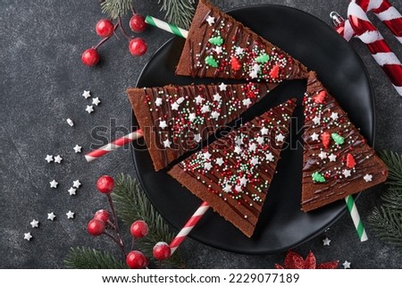 Chocolate brownies Christmas tree with chocolate icing and festive sprinkles on stone table. Christmas food ideas sweet homemade Christmas holidays pastry concept. Holiday cooking concept. Top view.
