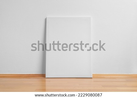 Clean art canvas leaning against a white wall. Parquet floor with reflection