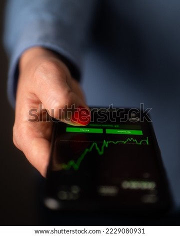 Female broker checking out the stock price on the smartphone. Price chart graphic going up. Buying stocks, investing, financial market, bull market. "Kaufen" (buy) and  "verkaufen" (sell) in German.