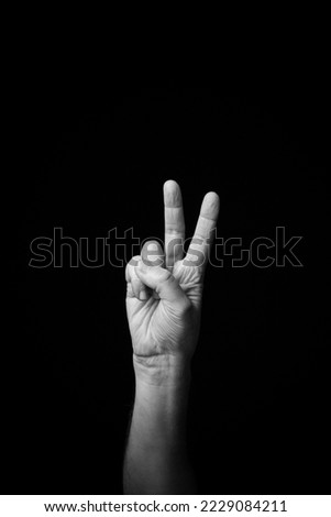 Dramatic black and white  image of a male hand fingerspelling the Fench sign language letter 'V', isolated against a dark background with copy space