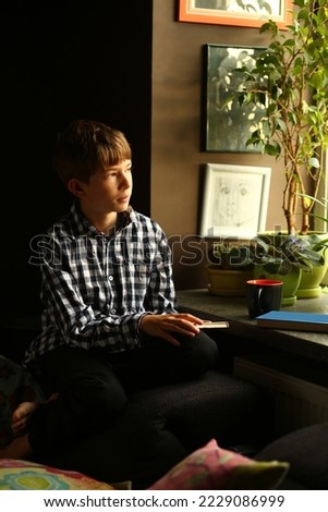 Indoor portrait of a boy dreaming and reading neat the window