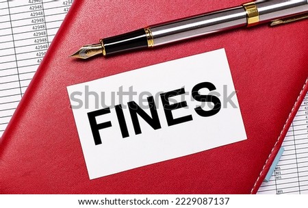 On the desktop there are reports, a burgundy notebook, a fountain pen and a white blank card with the text FINES. Business concept Royalty-Free Stock Photo #2229087137