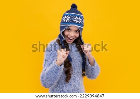 Beautiful winter kids portrait. Teenager girl posing with winter sweater and knit hat on yellow background. Excited teenager girl.