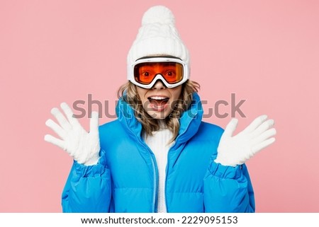 Snowboarder woman wear blue suit goggles mask hat ski padded jacket spend extreme weekend spread hands in gloves say wow isolated on plain pastel pink background. Winter sport hobby trip relax concept