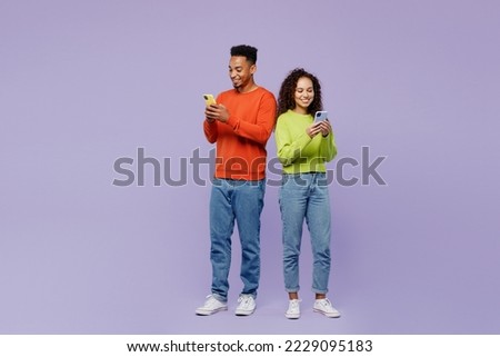 Full body fun young couple two friends family man woman of African American ethnicity wear casual clothes together hold in hand use mobile cell phone isolated on pastel plain light purple background