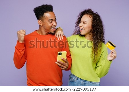 Young winner couple two friends family man woman of African American ethnicity wear casual clothes together use mobile cell phone credit bank card order delivery isolated on plain purple background