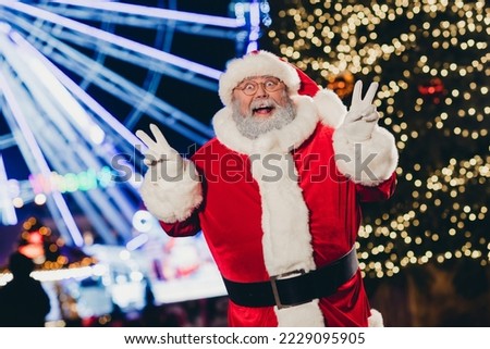 Portrait of excited funky santa grandfather two hands fingers demonstrate v-sign enjoy newyear time lights outdoors