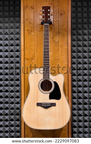 Wooden classic guitar with black figure on sounding board placed on wall of modern recording studio