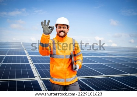 Portrait of smiling solar energy engineer showing okay sign and supporting renewable energy sources.