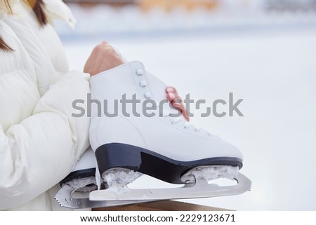 Woman holding ice skates outside in the winter near skating rink. Active lifestyle, dream concept.