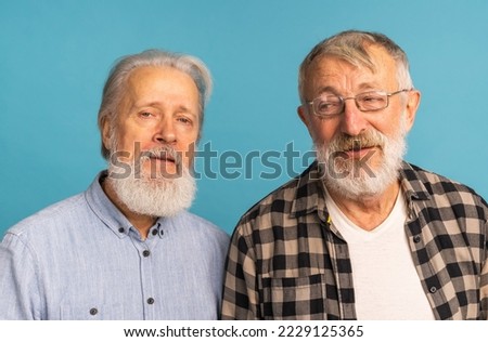 Portrait two elderly man friends standing over blue background - friendship, aged and senior people